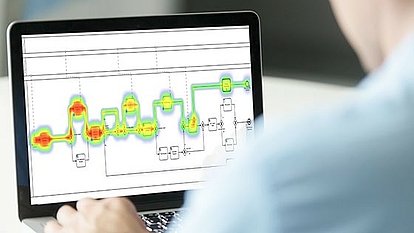 User Analyzing Workflow Diagram on Laptop A person using a laptop displaying a workflow diagram with a heatmap overlay, indicating areas of high and low activity.